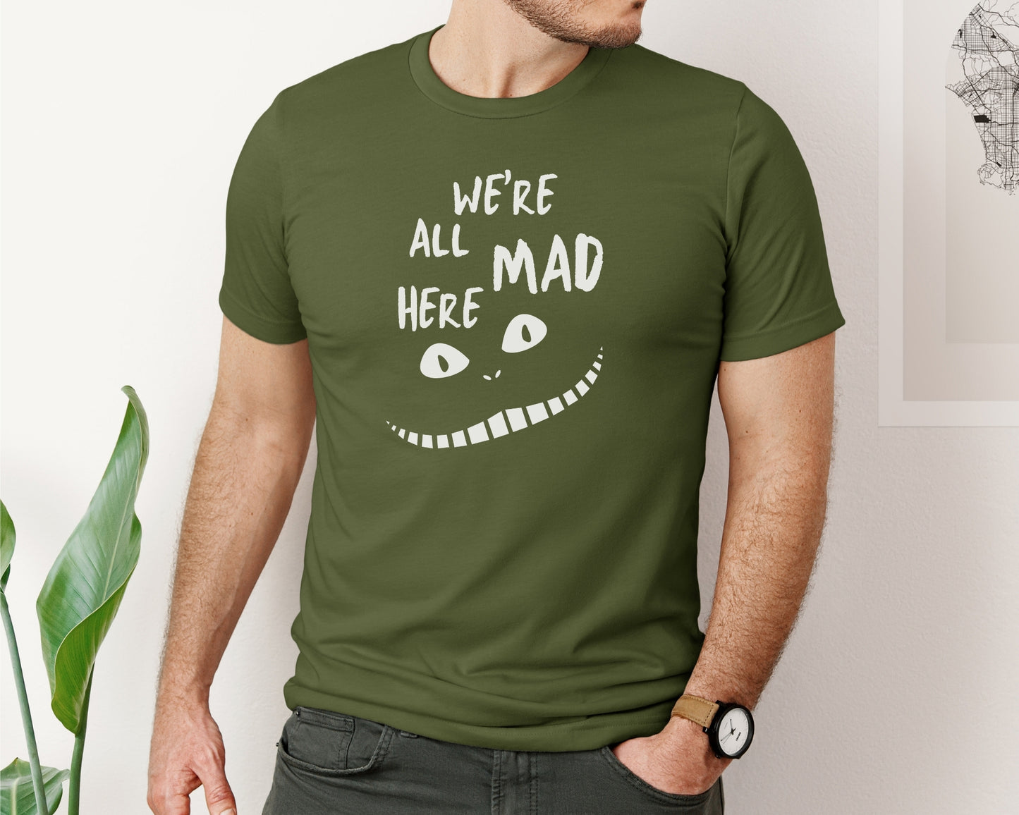 male model wearing bella and canvas 3001 t-shirt in olive with 'we're all mad here' cheshire cat inspired print on chest