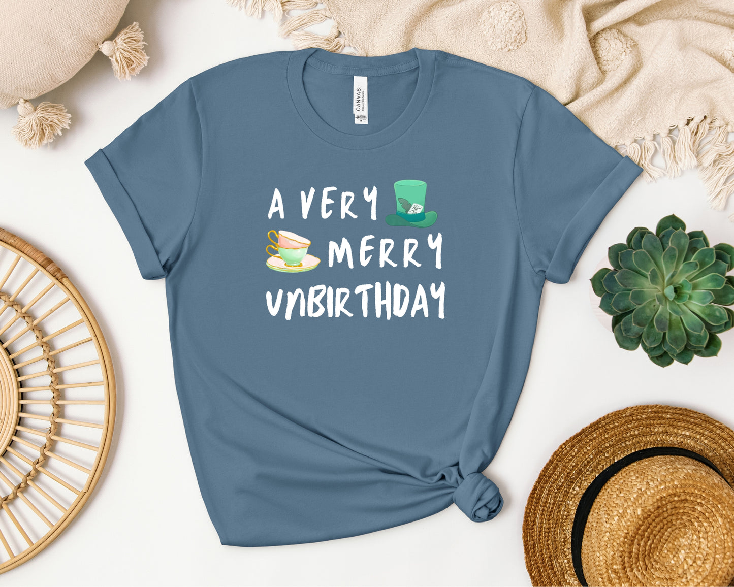 Bella and Canvas 3001 T-Shirt in steel blue laid flat, with a disney/Alice in Wonderland inspired 'a very merry unbirthday' design on chest