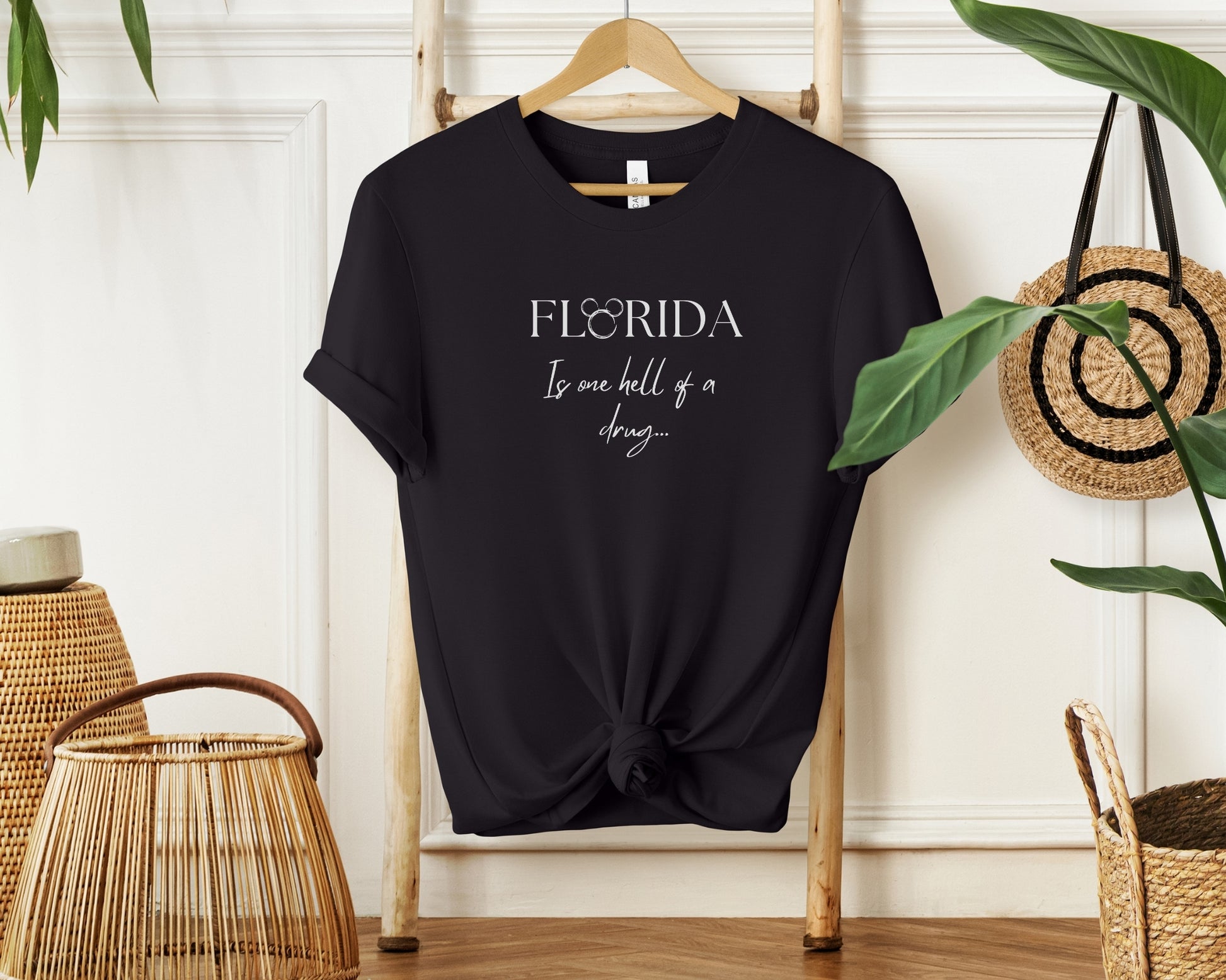 Hanging bella and canvas 3001 t-shirt in black with 'florida is one hell of a drug' disney x Taylor Swift inspired print on chest