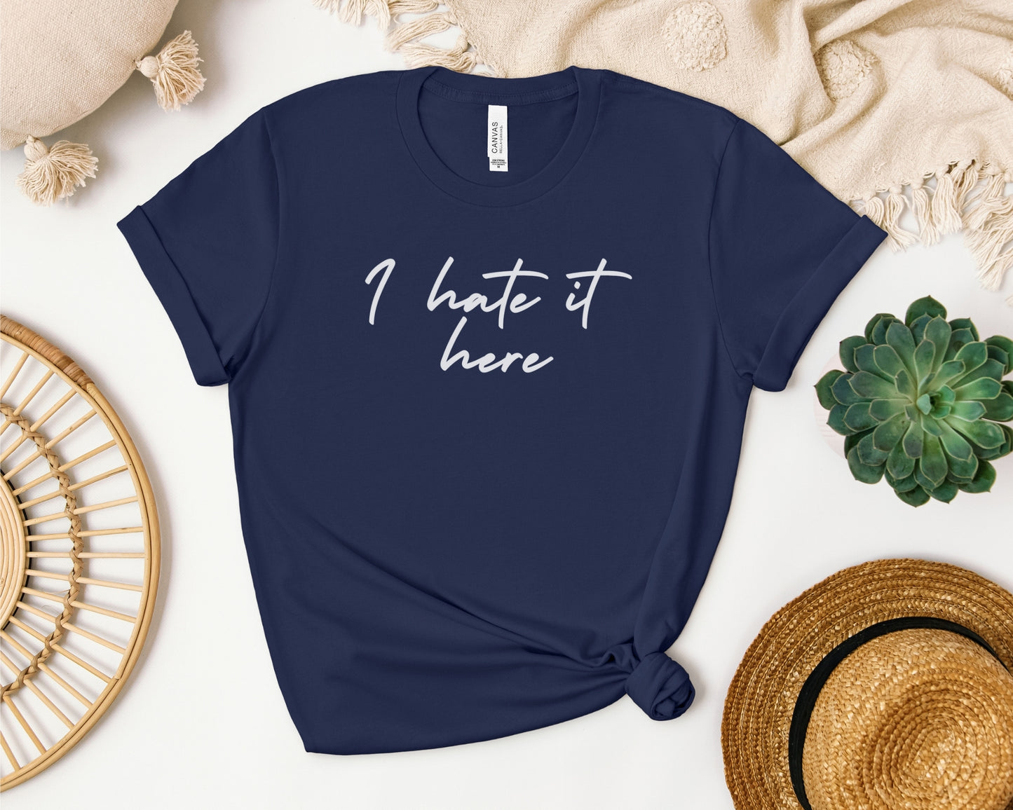 Bella and Canvas 3001 t-shirt in navy laid flat, with TTPD lyric print on chest, T-shirt has 'I hate it here' printed on chest in script style font inspired by Taylor Swift
